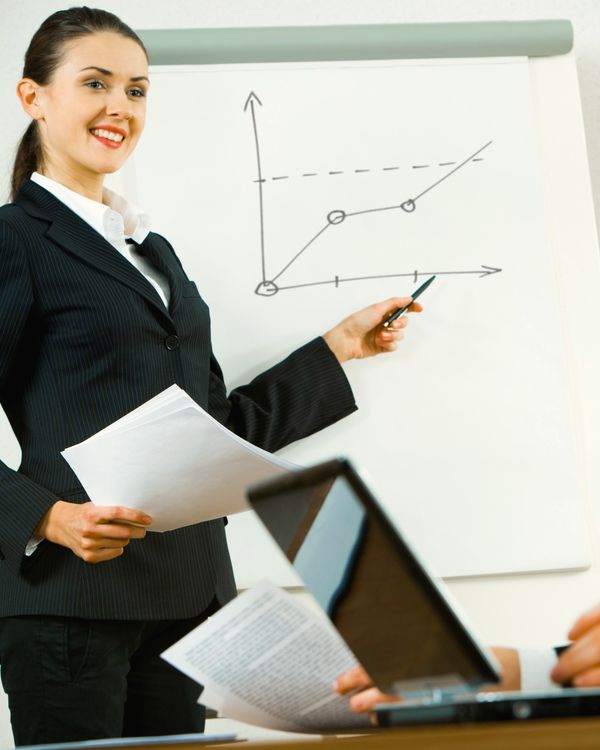 A woman points to a rising line on a flipchart while two colleagues listen