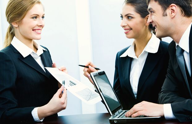 A woman shows a printed chart to two colleagues beside a laptop
