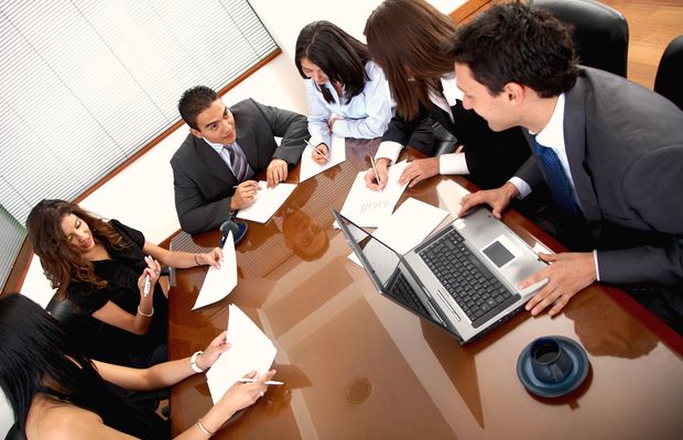 Six colleagues work around a polished meeting table with laptops and papers