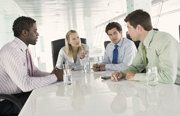 Four colleagues talk across a white table in a bright meeting room