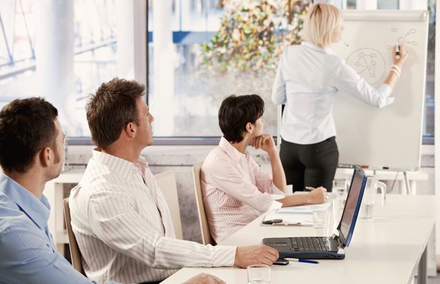 A woman sketches on a flipchart in front of three colleagues at a meeting table